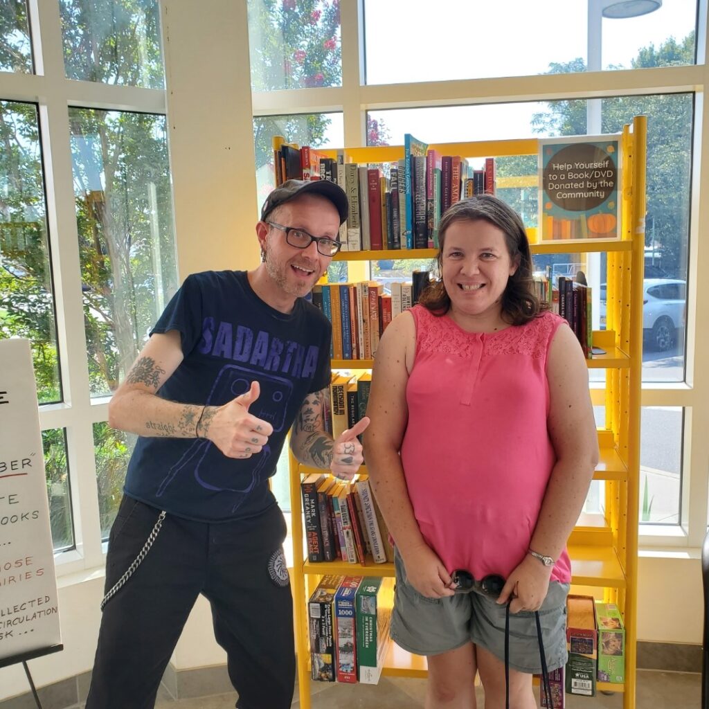 Elaine and DSP John in front of a book shelf at the library