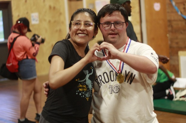 A Camp Loyaltown counselor and camper form a heart together using one hand each.