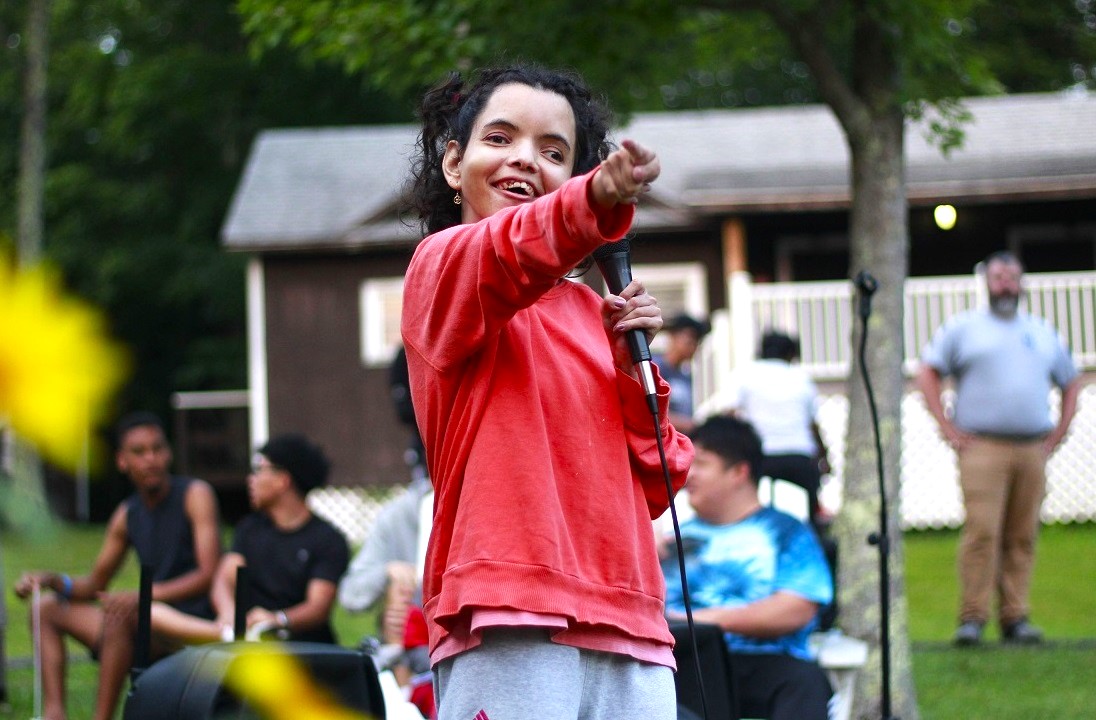 A Camp Loyaltown camper holds a microphone and points out during a performance