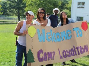 Three Camp Loyaltown campers hold a hand painted sign reading "Welcome to Camp Loyaltown"