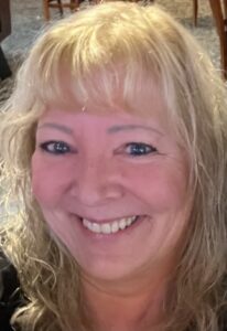 Close-up portrait of a smiling woman with shoulder-length blonde hair.