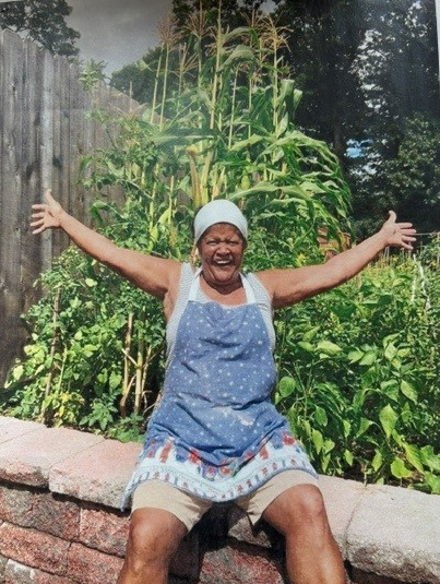 Rosa Green sits with her arms outstretched in front of the Helen Kaplan Garden