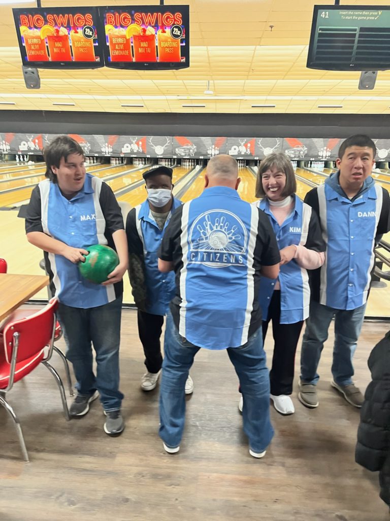 People supported by Citizens show off their bowling shirts at the bowling alley