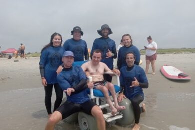 Noah poses with Camp Anchor volunteers as he tries surfing