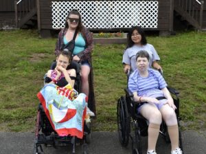 Two campers in wheelchairs and two staff members pose for a photo