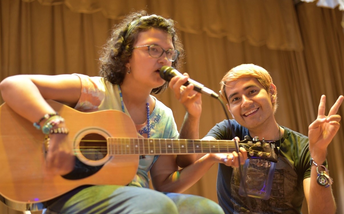 A camper plays guitar and sings while a counselor holds the microphoner