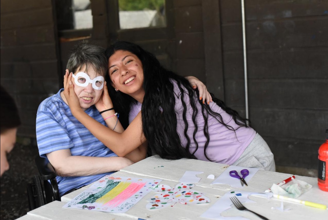A Camp Loyaltown counselor helps a camper wear paper glasses that she made during craft time