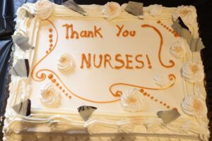 A vanilla frosted cake with "Thank You NURSES!" written in orange icing.