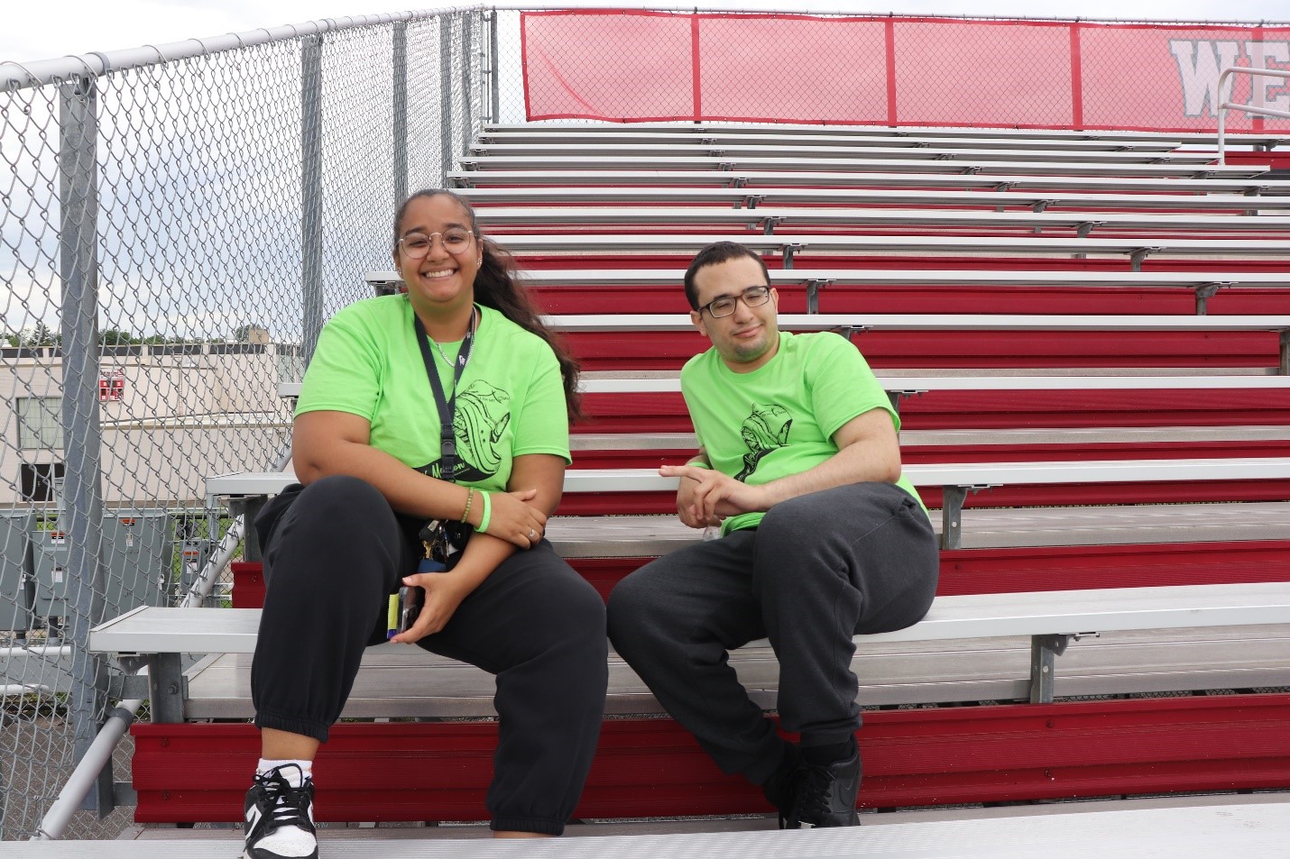 Direct Support Professional Briana Brito and Resident Christian Rios sitting on the bleachers during the Hope N' Motion Walk-a-Thon in support of youth mental health.