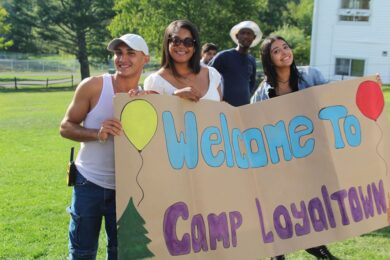 Three Camp Loyaltown campers hold a hand painted sign reading "Welcome to Camp Loyaltown"